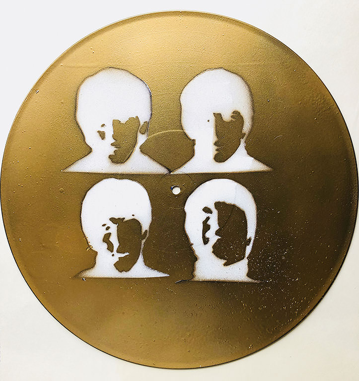 Gold painted disk with four silhoutted heads.