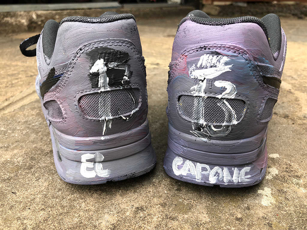 Heel view of a pair of purple painted shoes. One says El the other Capone.